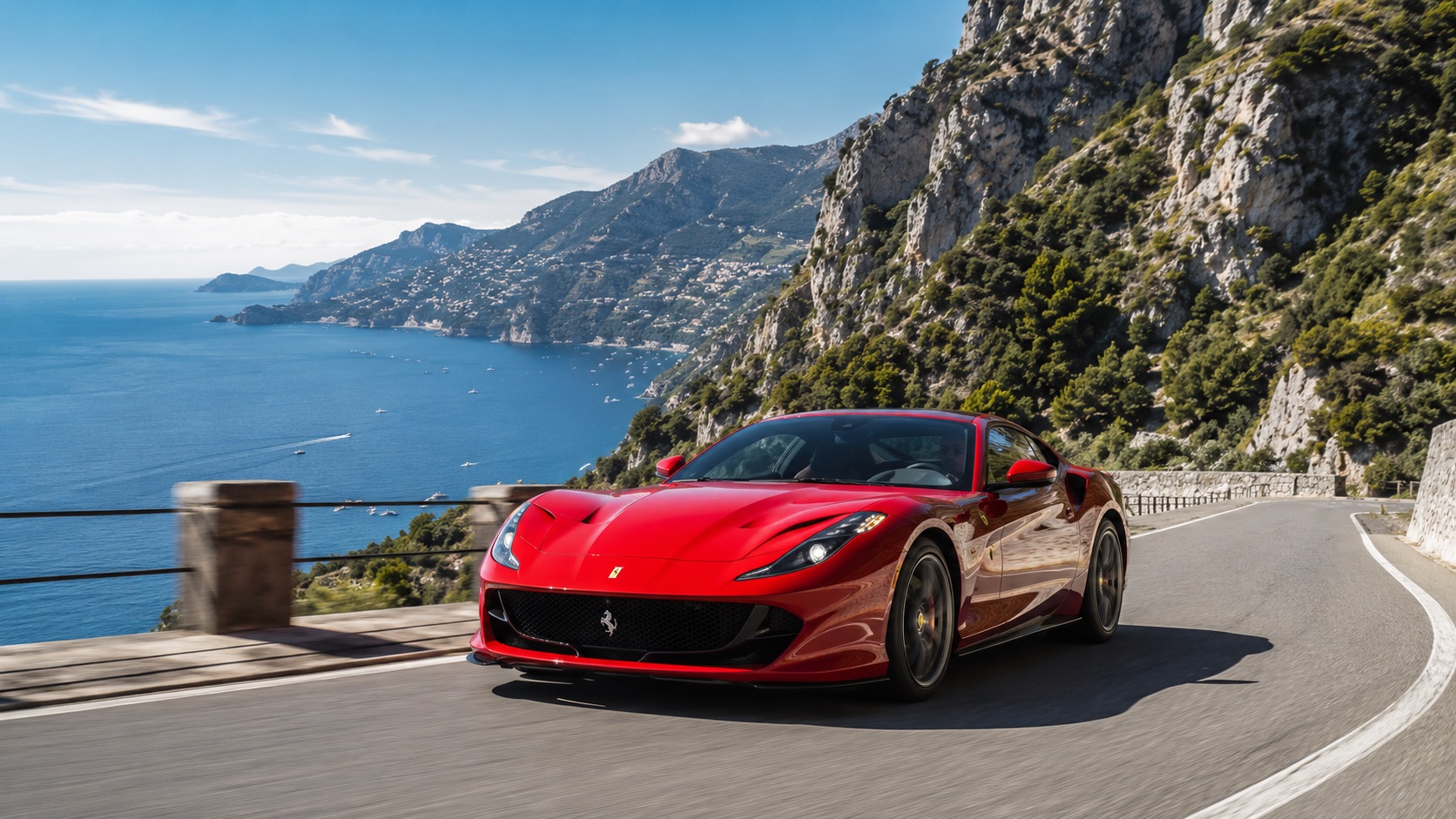 Red luxury sports car driving along a scenic coastal mountain road.